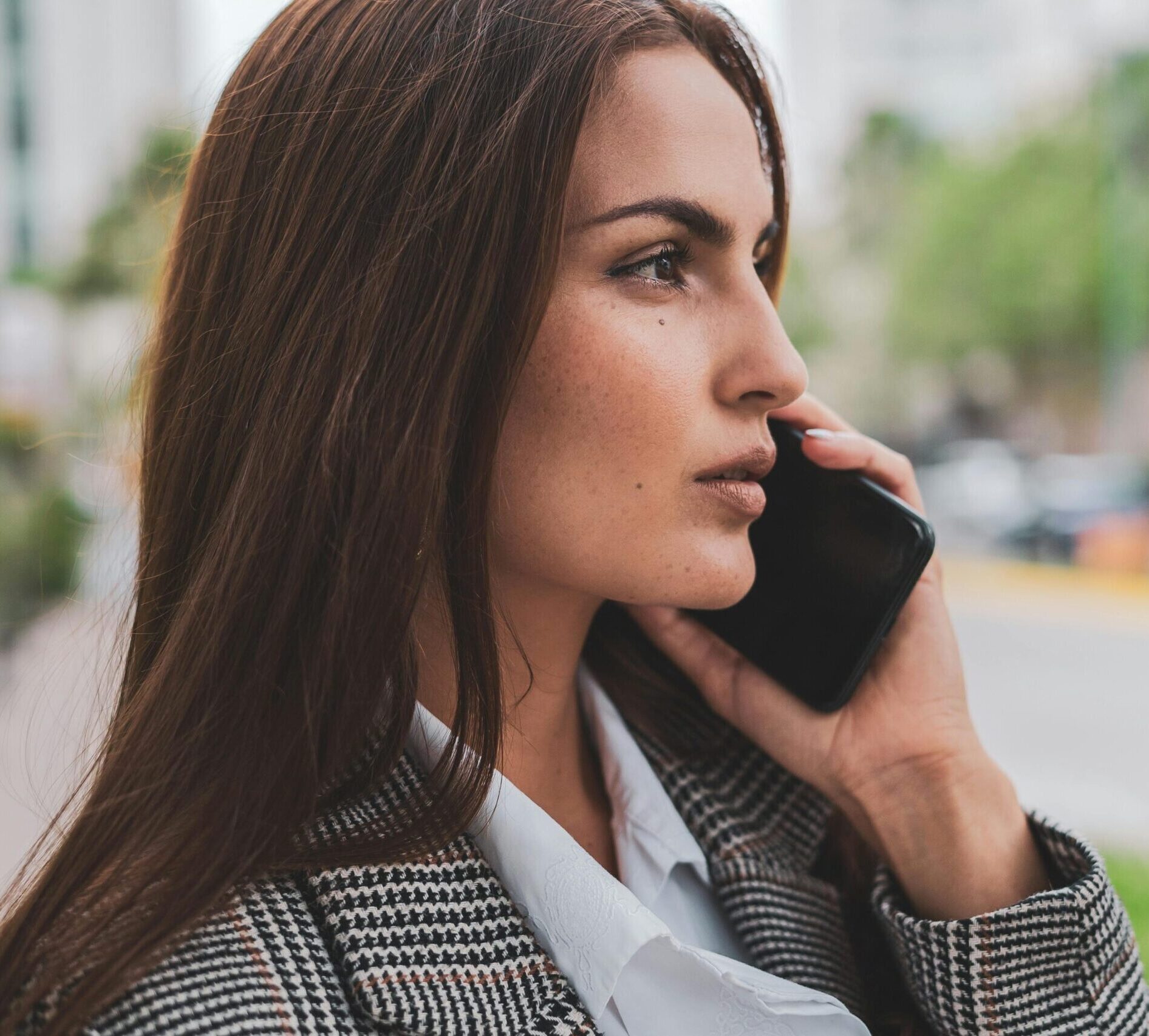 Confident businesswoman with brown hair talking on smartphone outdoors.